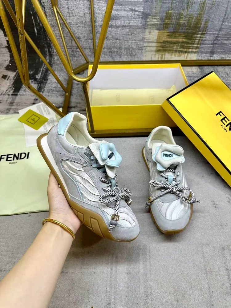 FENDI Wave Pulse繫帶低幫運動鞋。淺灰色緞面材質，飾有褶襉和同色系絨面革嵌飾。淺藍色皮革後跟鞋領。鞋舌為可拆卸摺疊式設計，飾有立體同色花冠飾片。彈力鞋帶搭配拼色管狀鞋帶，點綴淺藍色珠飾及飾有金色FF圖案的立方元素。鞋側與鞋舌飾