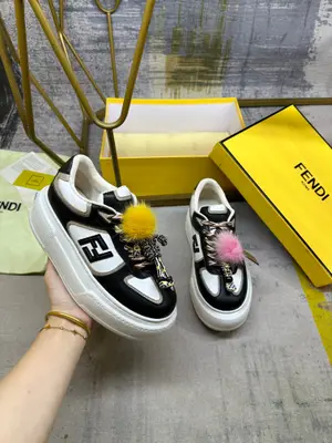 FENDI Match繫帶運動鞋。黑白色皮料側面飾有黑色皮革FF貼花，拼色鞋帶。橡膠厚鞋底，後跟處飾有超大凸紋FENDI字樣。鞋舌上飾有金屬環掛飾：右鞋上飾有帶黃色貂皮細節和金色金屬FF圖案手鍊的編繩小玩偶。左鞋上飾有一條帶撞色貂毛雙絨球的