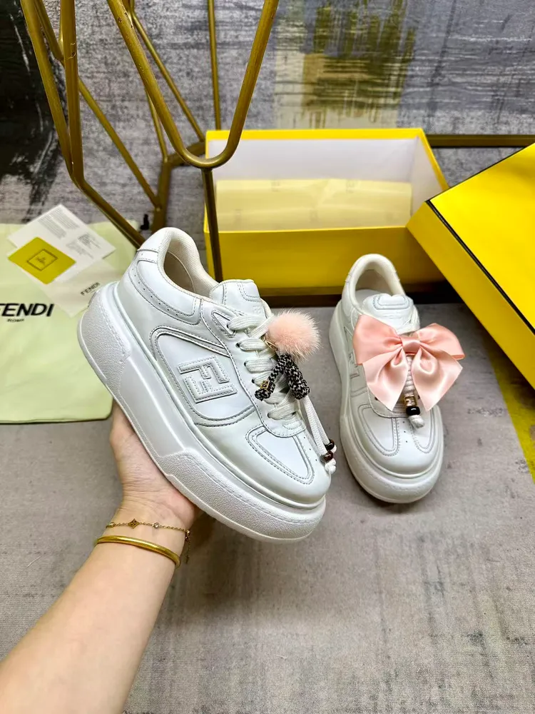 FENDI Match繫帶運動鞋。白色皮革材質。側面飾有同色系皮革FF貼花，配白色鞋帶。橡膠厚鞋底，後跟處飾有超大凸紋FENDI字樣。鞋舌上飾有金屬環掛飾：右鞋上飾有帶粉紅色貂皮細節和金色金屬FF圖案手鍊的編繩小玩偶。左鞋上飾有配白色和粉紅